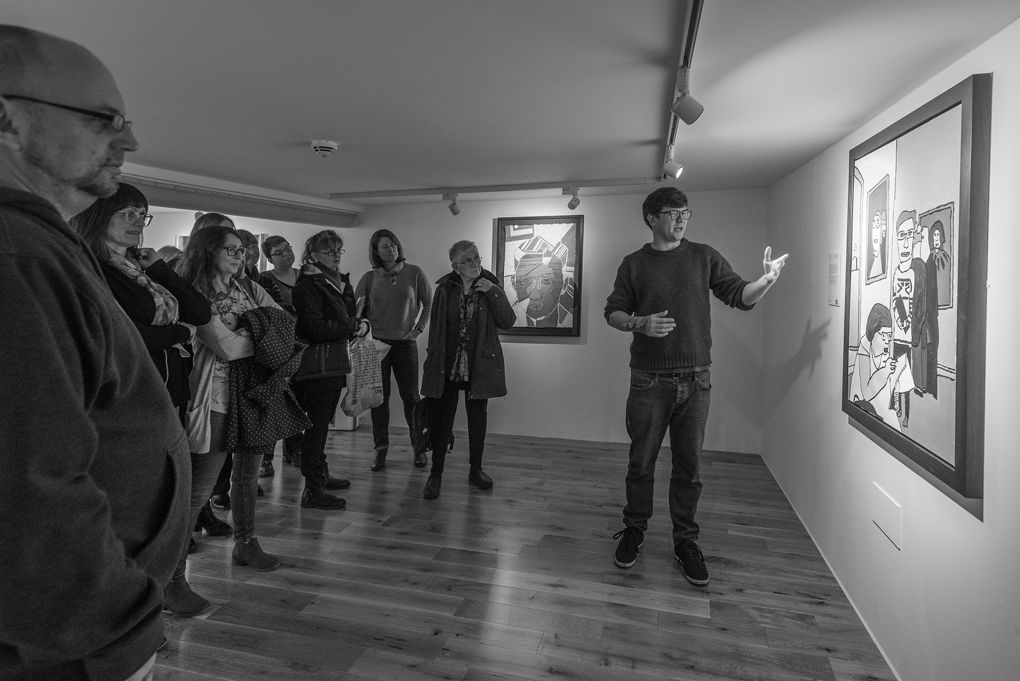 A man presents a painting in a gallery to a small crowd of people