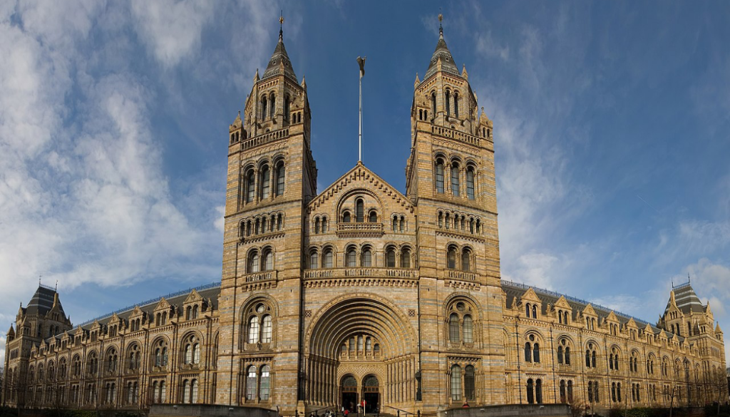 A panoramic image of the Natural History Museum in London. The image shows a large, Victorian building with 2 towers flanking a large arched doorway.